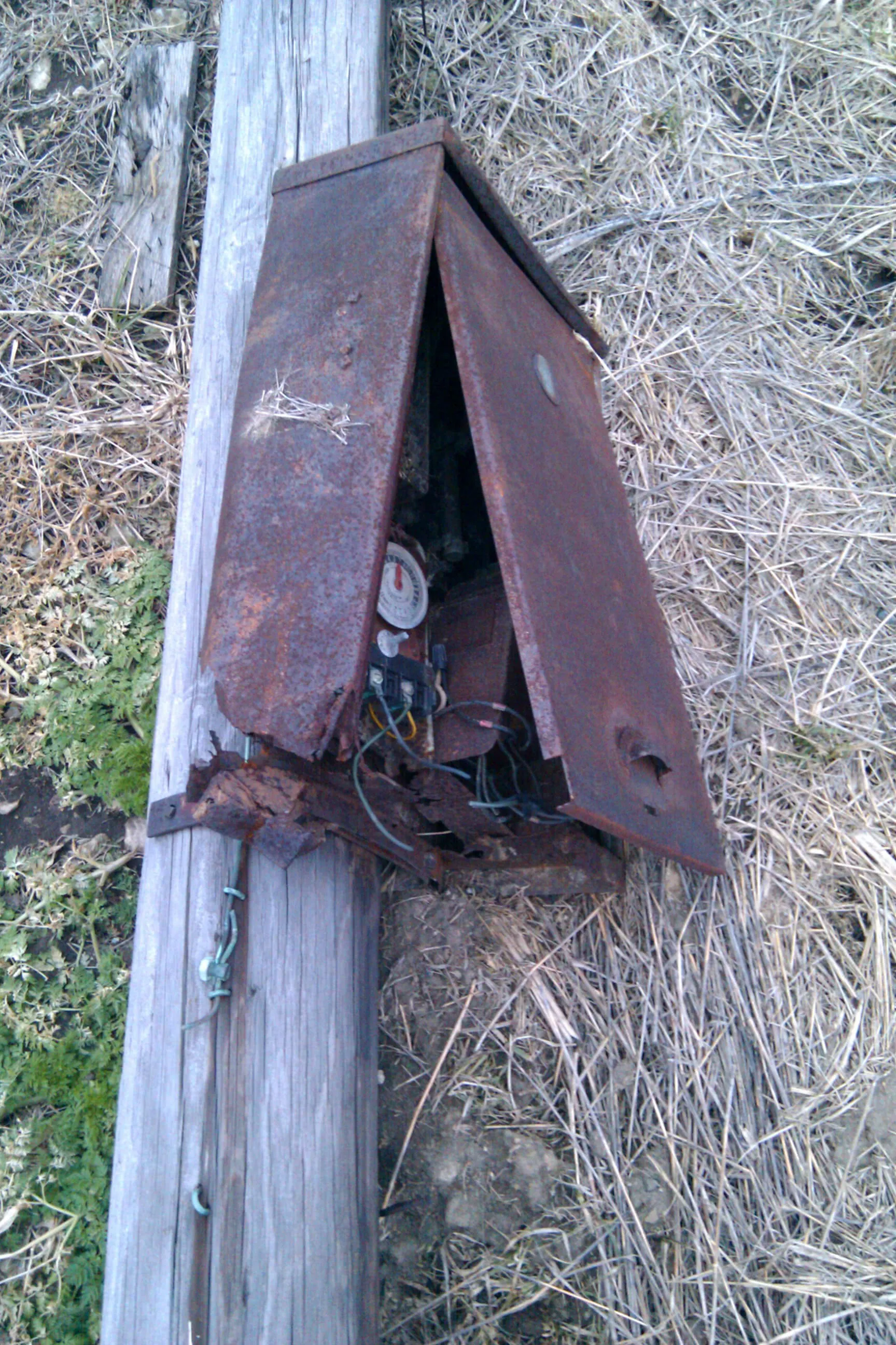 a rusting, broken meter box on a felled pole