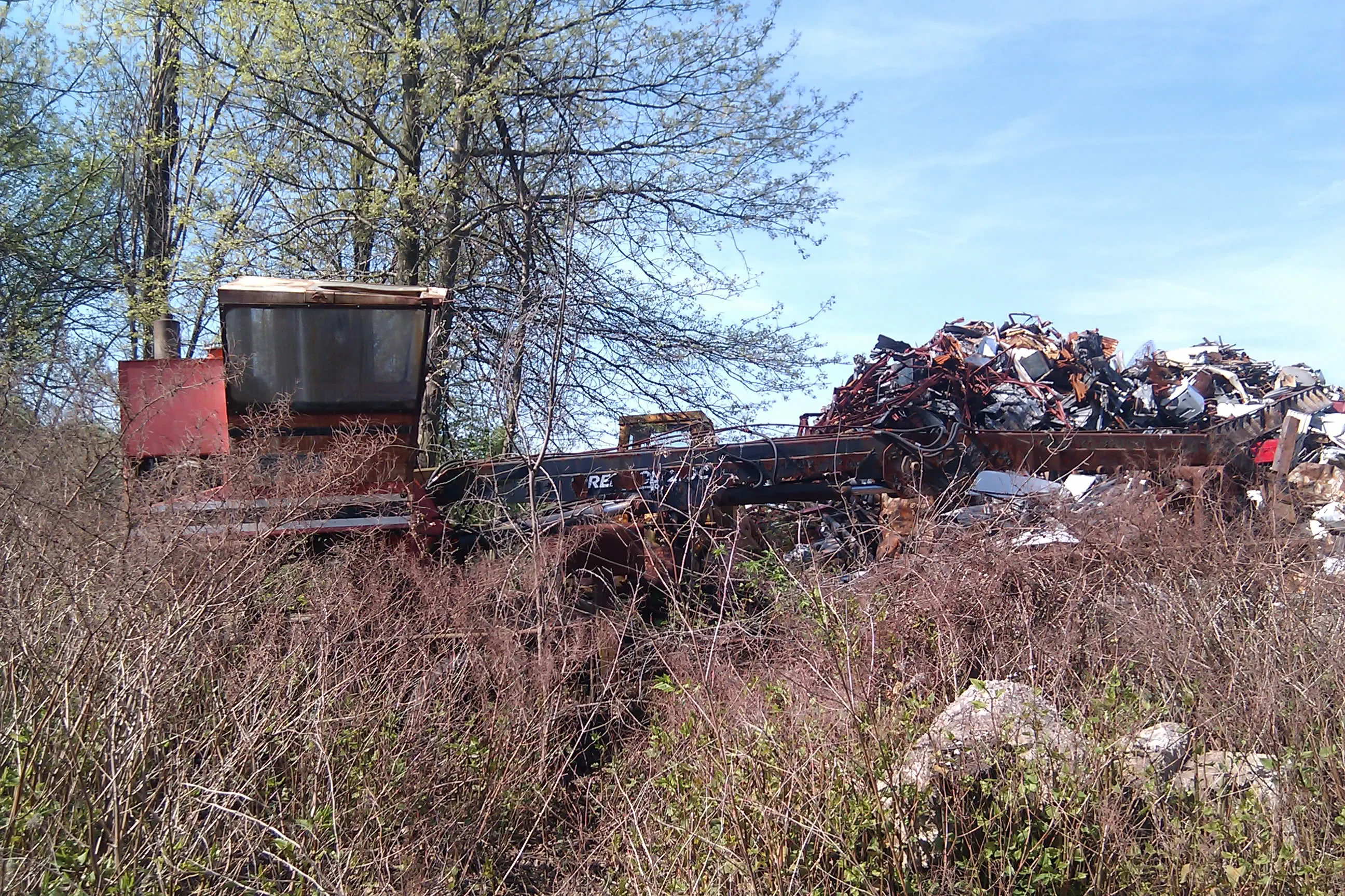 a bunch of random metal and tractor parts covered by weeds